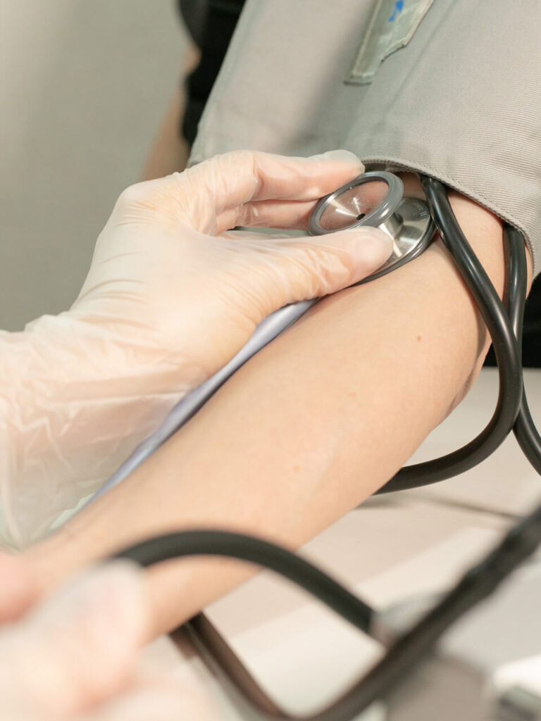 医療用手袋を着けたスタッフが血圧計で腕の血圧を測定している様子