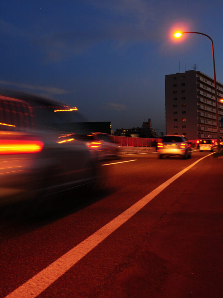 夕暮れ時の道路を車が走行し、街灯が灯っている風景